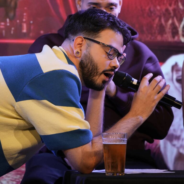 Comedian in glasses and a striped polo shirt speaking close to the microphone