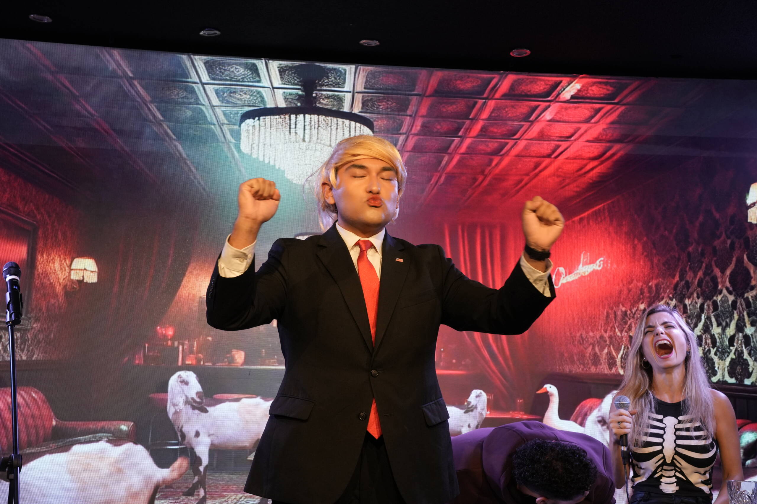 Performer in a suit and blond wig raising both fists on stage