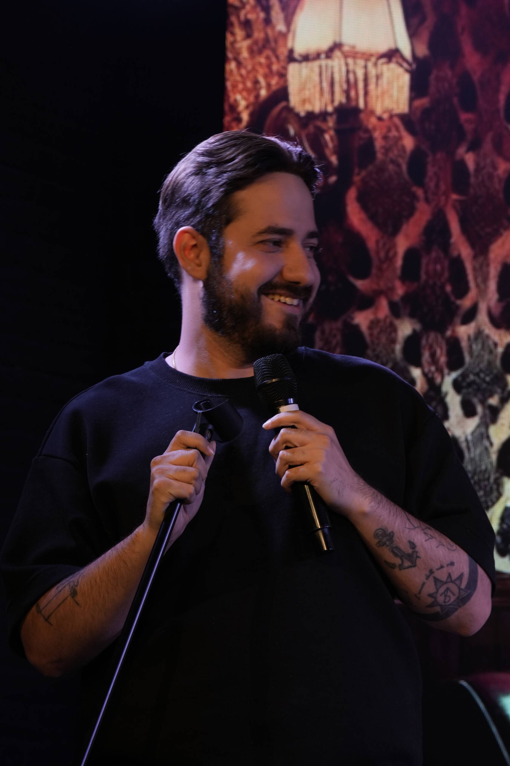 Comedian in a black T-shirt smiling at the microphone