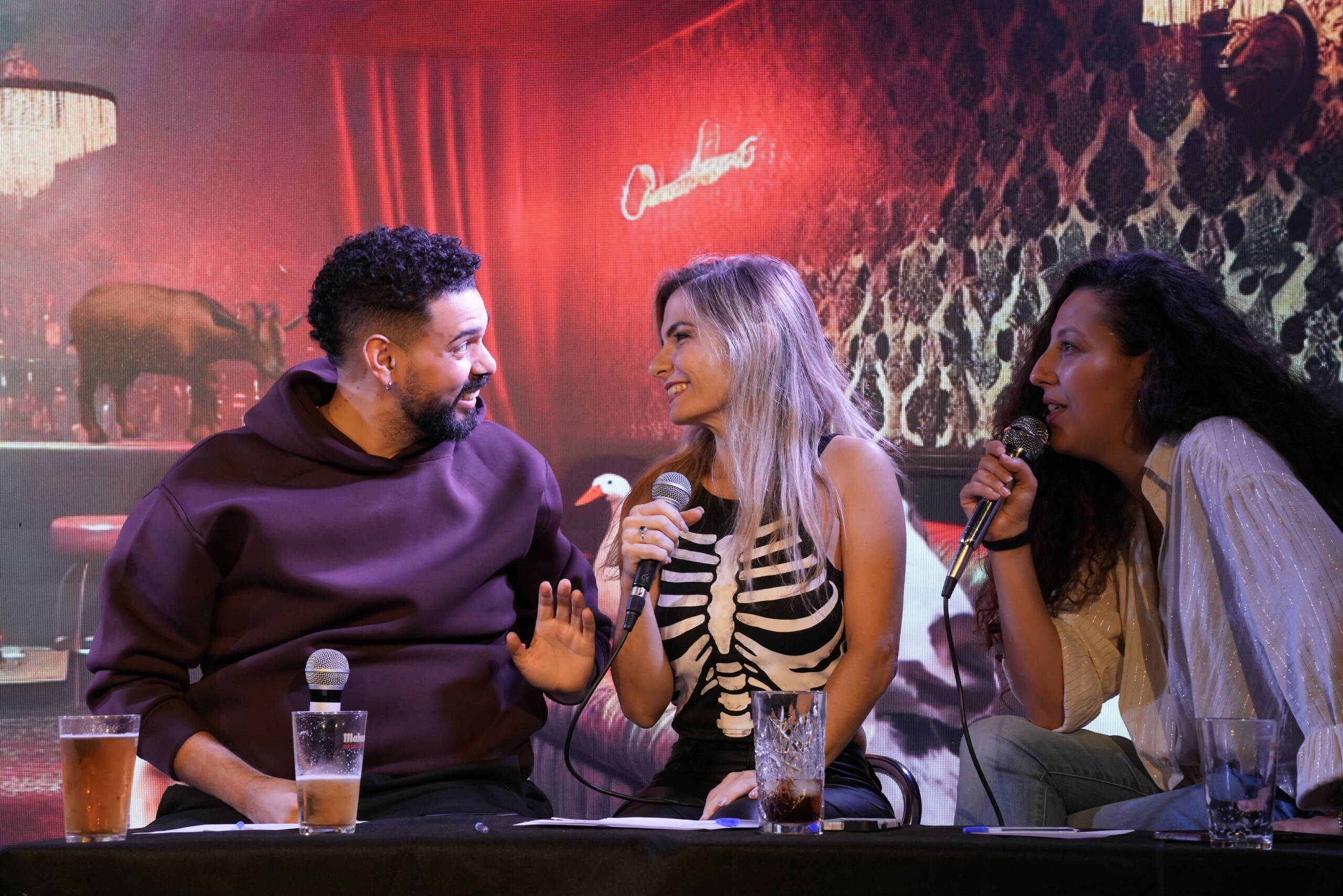Three performers laughing together at a table on stage
