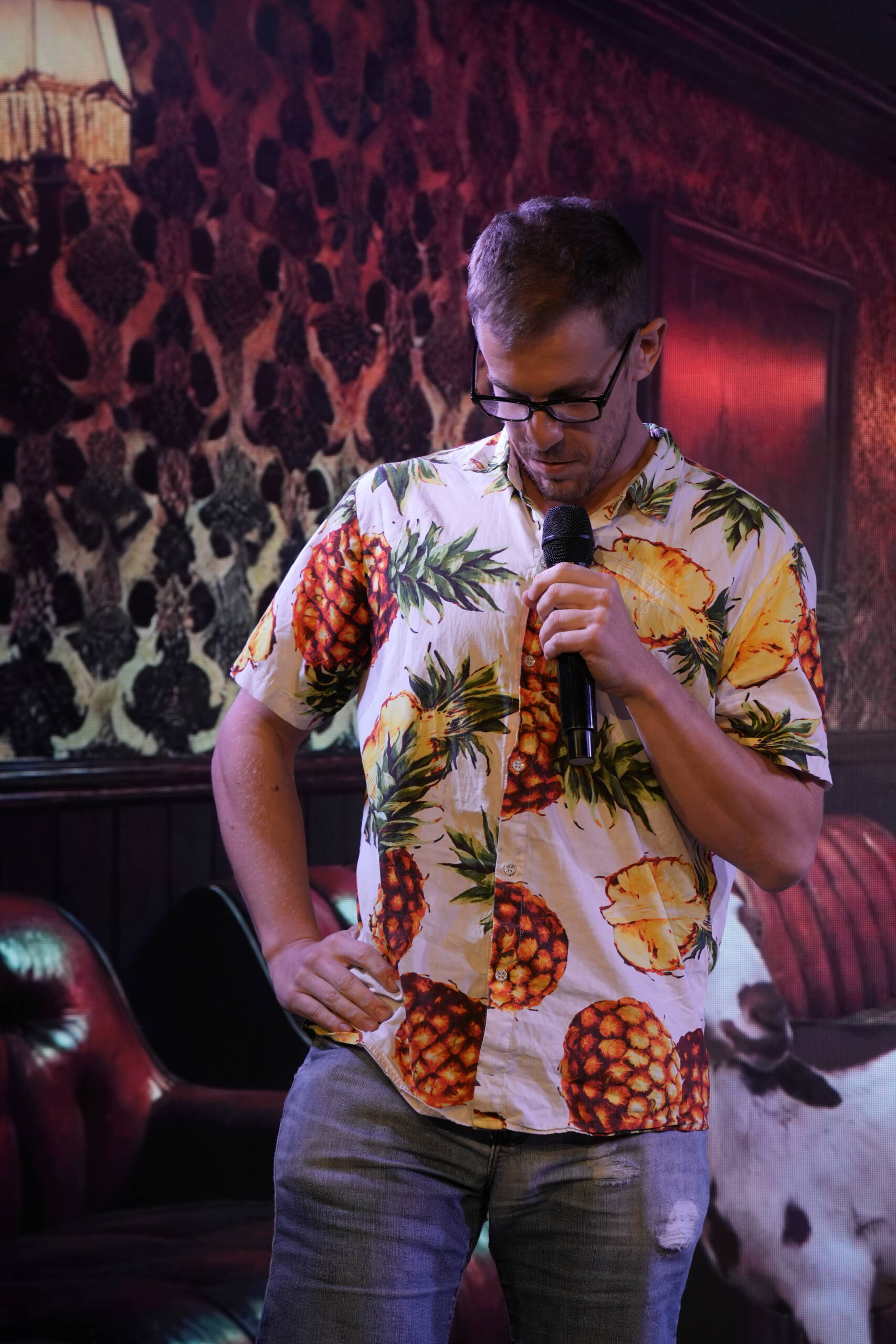 Comedian in a pineapple-print shirt looking down at the microphone