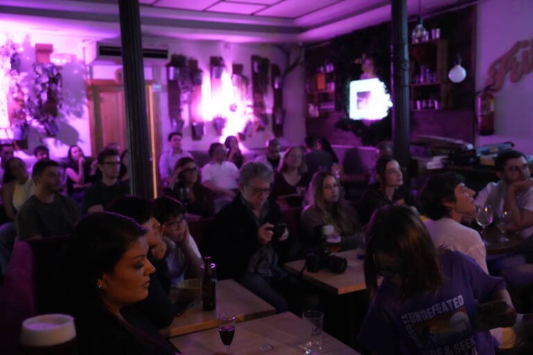 Audience packed around tables under purple light