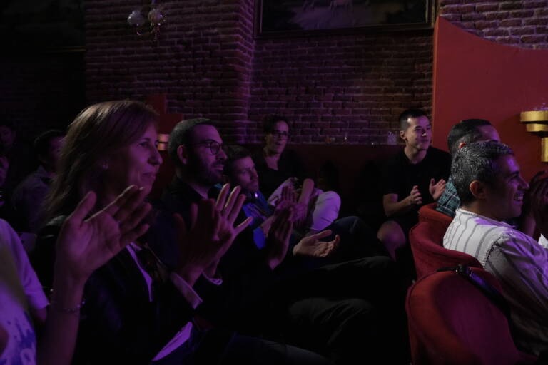 Audience members laughing and clapping in a dark room