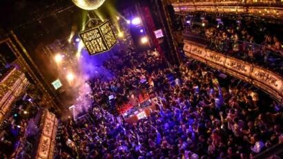 Aerial view of a packed multi-level nightclub, with a crowd under purple lights