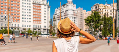 A woman in a straw hat seen from behind, looking at large buildings in a sunny Madrid square