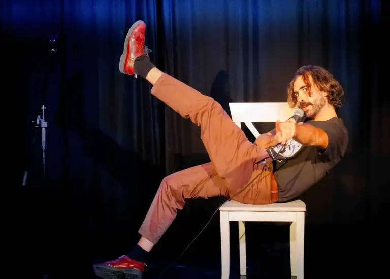 Comedian lying back in a white chair with one leg in the air
