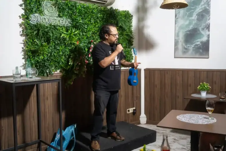 Comedian holding a blue ukulele and a microphone at Tropicana