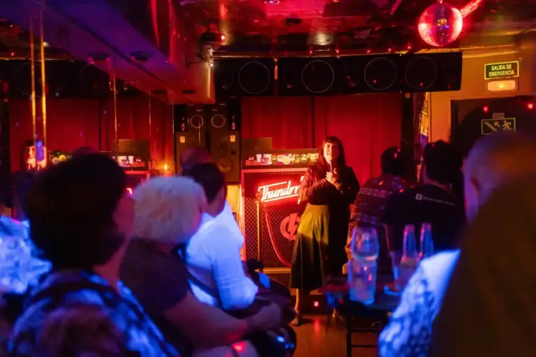 Comedian performing in a small red-lit room packed with audience