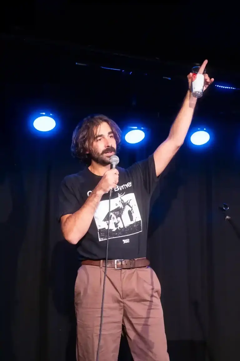 Comedian raising an arm while performing under blue stage lights
