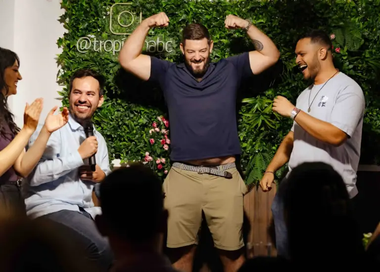 Comedian flexing for the crowd while two other performers laugh, at Tropicana